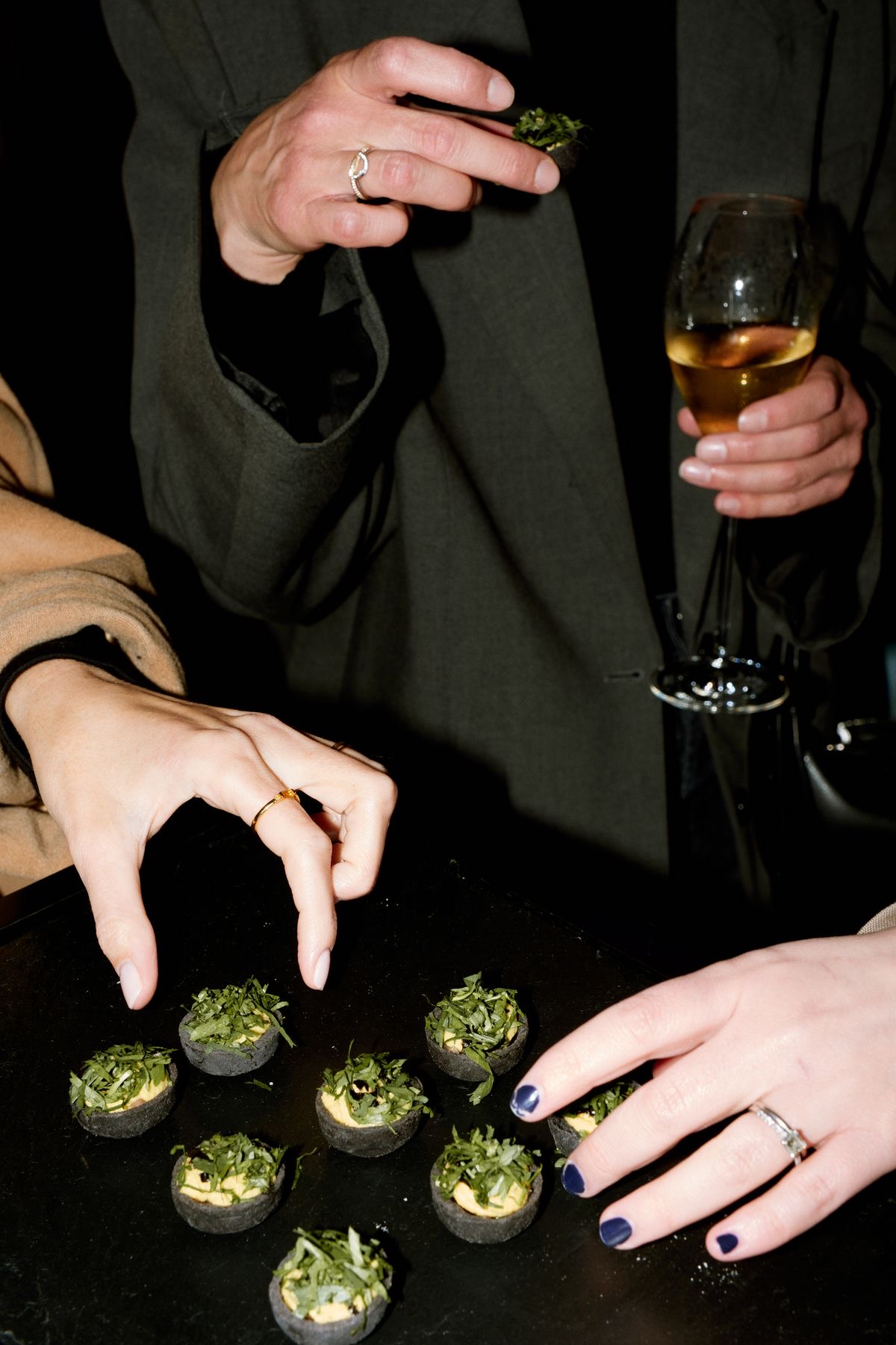 An elegant reception table lined with martini glasses and small-bite cups, guests gathered in a modern architectural space