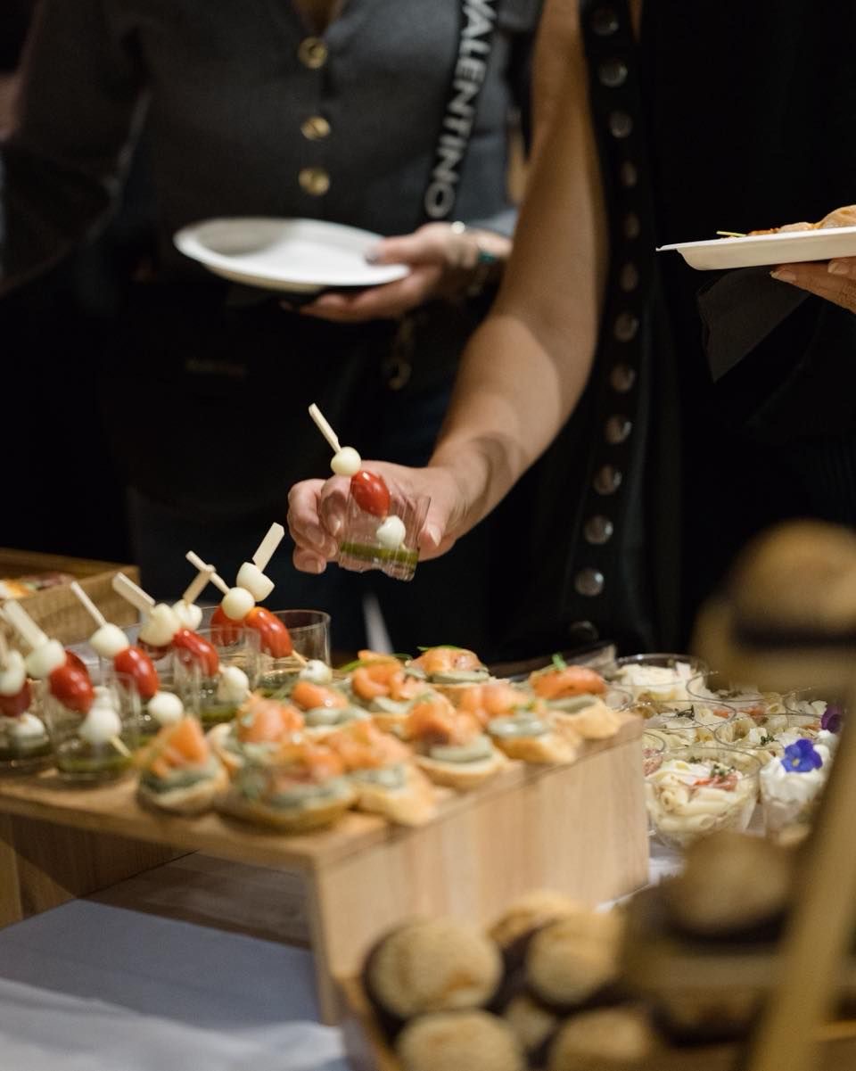 A server offering caprese skewers and salmon canapés from a wooden display at an event
