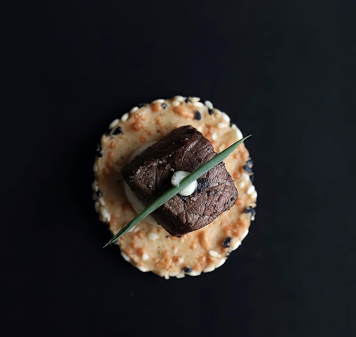 A single seared beef canapé on a crisp cracker, photographed from above on a dark surface