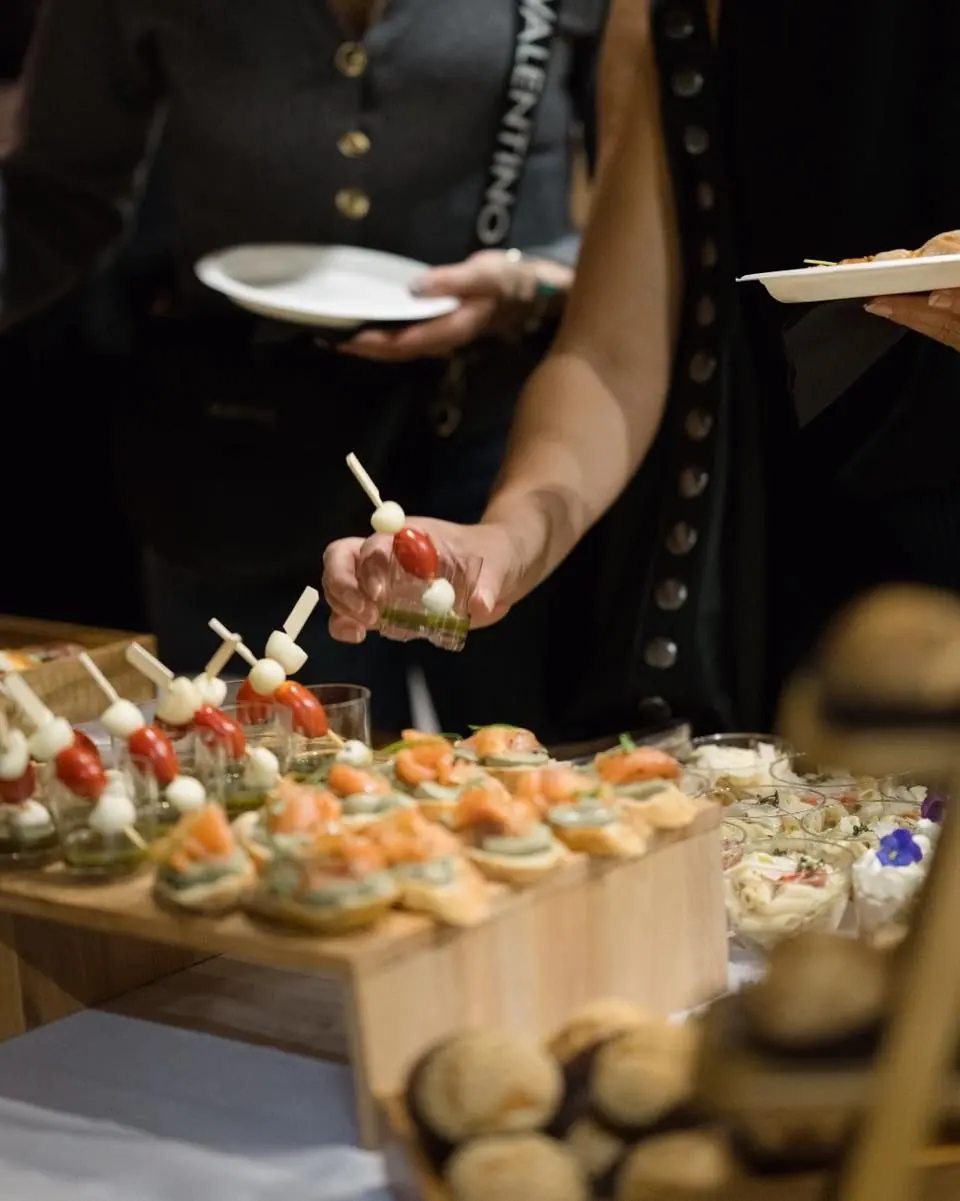 A server offering caprese skewers and salmon canapés from a wooden display at an event