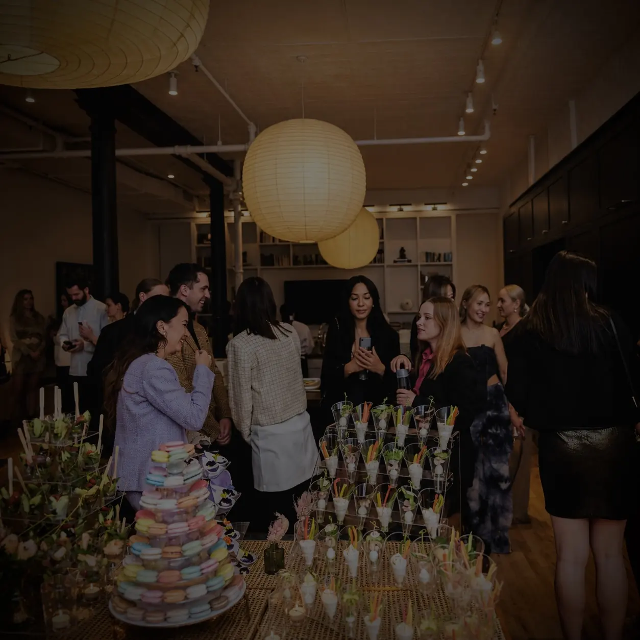 Guests gathered in an elegant loft space around beautifully arranged catering displays and glowing paper lanterns