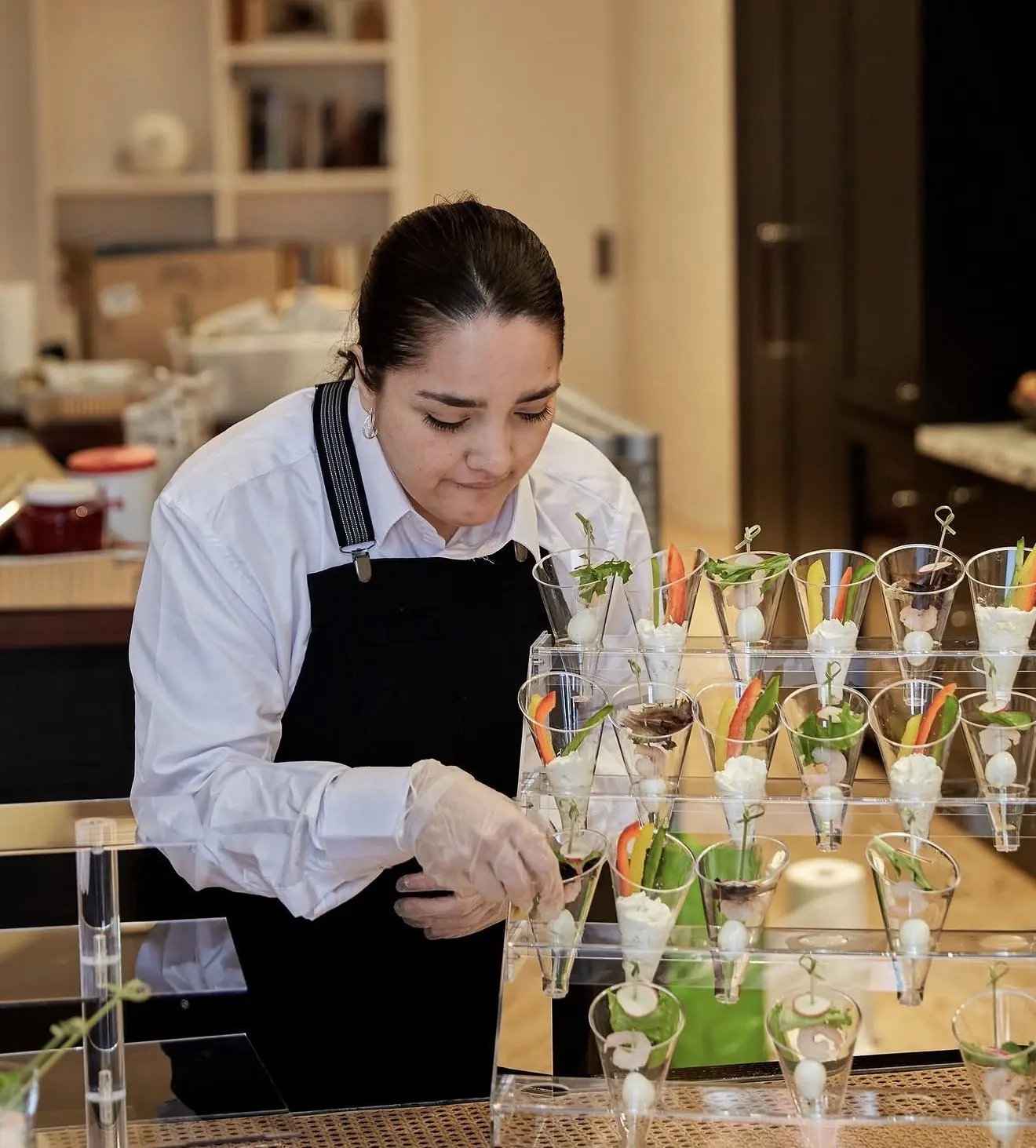 A host carefully arranging elegant small-bite cups in a warm, intimate setting with soft ambient light